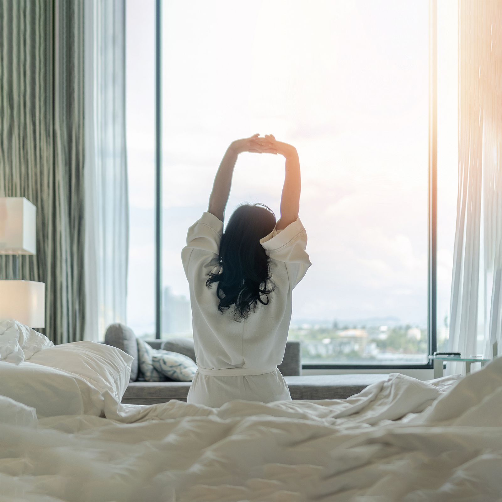 Easy lifestyle Asian woman waking up from good sleep in weekend morning taking some rest, relaxing in comfort bedroom at hotel having happy lazy day enjoying work-life quality balance concept